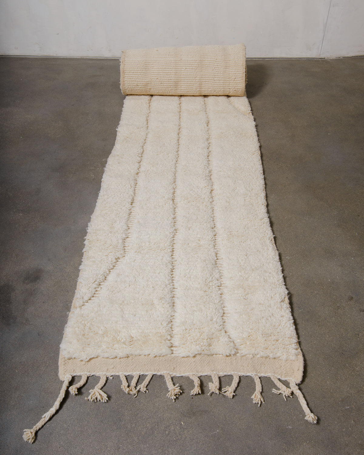 Long Berber runner rug in soft cream wool, half rolled out on grey concrete floor.